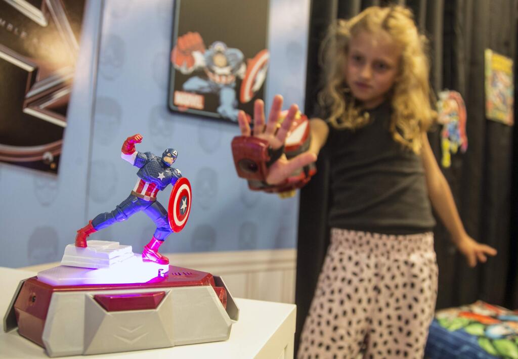 In this Friday, May 29, 2015 photo, actress Evangeline Lindes role demonstrates a Playmation 'repulsor' a wearable forearm attachment that puts kids in the role of Marvel superhero Iron Man, that connects via sensors with a base station called a ìpower activator,î at left, at the Disney Consumer Products offices in Glendale, Calif. Disney is launching its new Playmation line of toys that combine high-tech wearable gadgets and old-school superhero role-playing to keep kids moving while engrossing them in sub-plots from ìThe Avengers,î ìStar Warsî and ìFrozen.î (AP Photo/Damian Dovarganes)