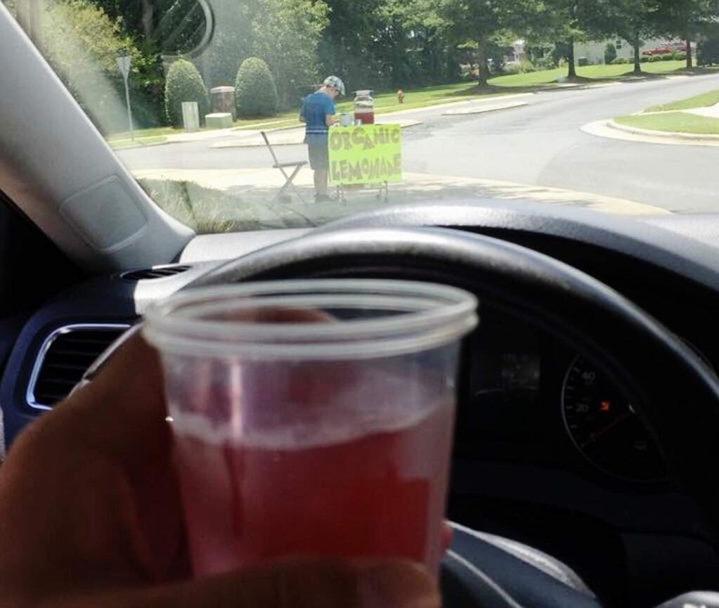 This Saturday, Aug. 4 2018, photo provided by James Castellano, of Monroe, N.C., shows a drink he bought from a boy, background, in Monroe. A teenager who held up the North Carolina lemonade stand for $17 was still at large Monday, Aug. 6, and authorities said they hoped to track him through surveillance footage and possible DNA and fingerprint tests. (James Castellano via AP)