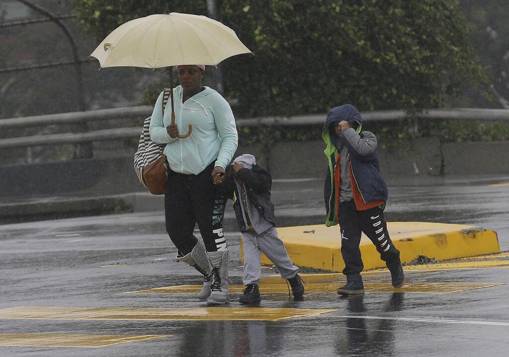 A woman carries an umbrella as she crosses a street with children in San Francisco, Tuesday, Feb. 7, 2017. Flash flood watches are in place for parts of Northern California down through the Central Coast as heavy rains swamp roads and threaten to overtop rivers and creeks. (AP Photo/Jeff Chiu)