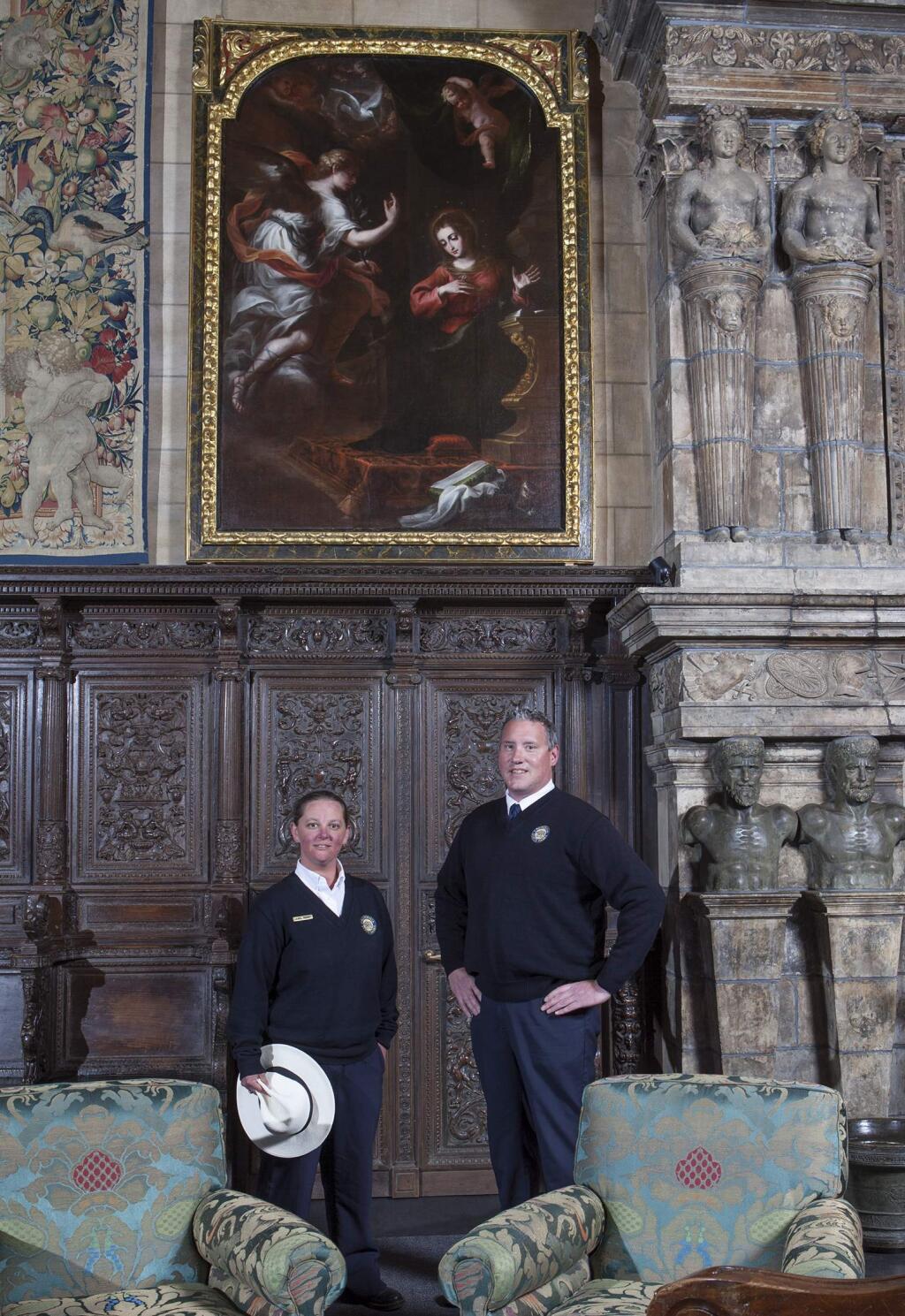 In this undated photo provided by Hearst Castle/California State Parks are guides Laurel Rodger and Carson Cargill posing below the 'Annunciation' painting hanging at Hearst Castle in San Simeon, Calif. The painting, that has been hanging at California's landmark Hearst Castle for decades, has been identified as a 17th century work thanks to two guides who noticed a previously undetected monogram and inscription when it was illuminated by late afternoon sunlight last fall. (Victoria Garagliano/Hearst Castle/California State Parks via AP)