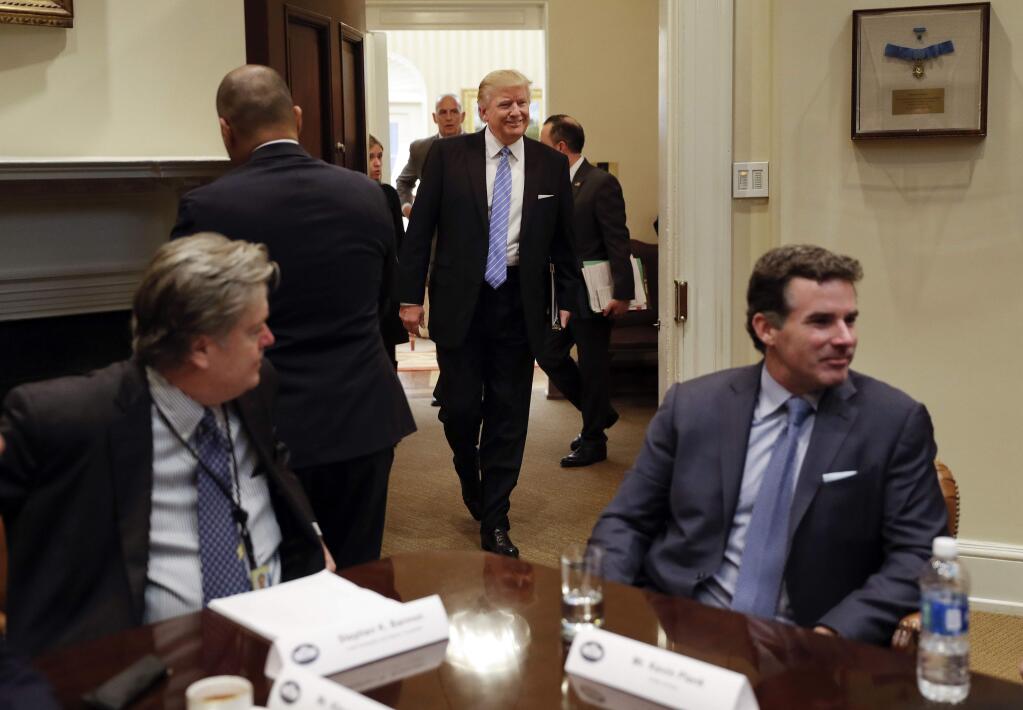 FILE - In this Jan. 23, 2017, file photo, President Donald Trump smiles as he walks in from the Oval Office of the White House in Washington, to host breakfast with business leaders in the Roosevelt Room. Sitting at the table are then-White House senior adviser Steve Bannon, left, and Kevin Plank, founder, CEO and Chairman of Under Armour. Trump returned fire with both barrels Wednesday against criticism leveled at him in a new book that says he never expected - or wanted - to win the White House, his victory left his wife in tears and a senior adviser thought his son's contact with a Russian lawyer during the campaign was 'treasonous.' (AP Photo/Pablo Martinez Monsivais, File)