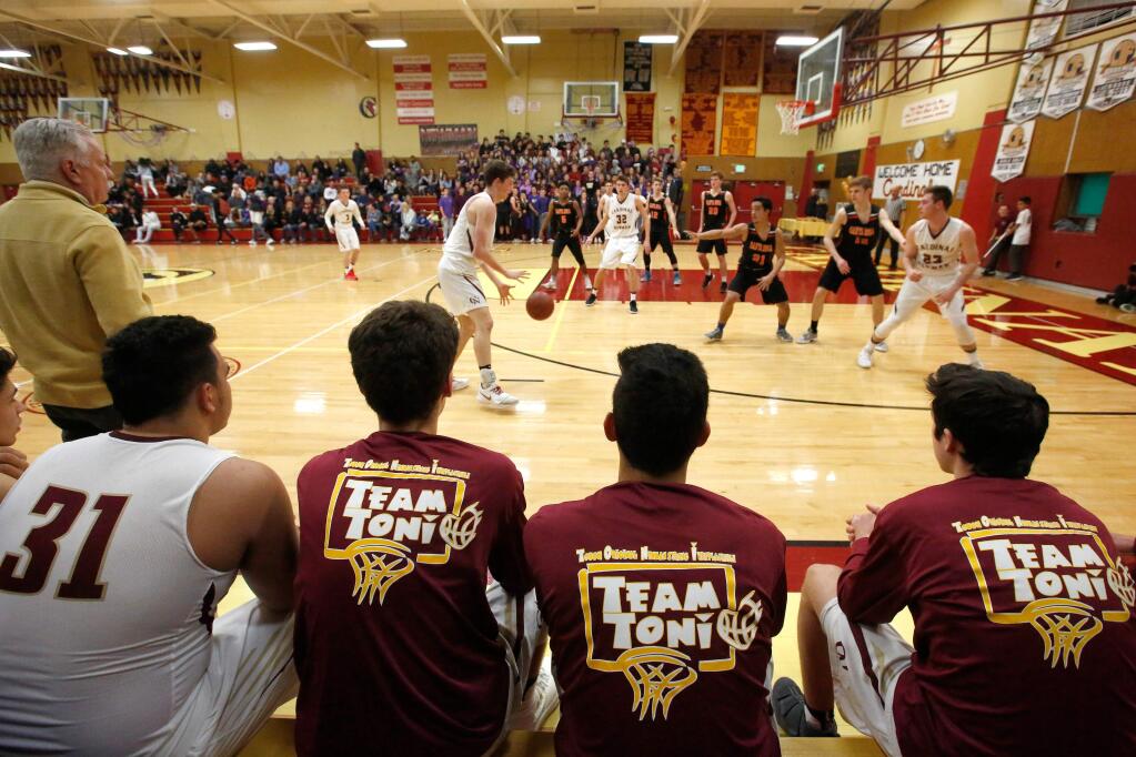 Cardinal Newman's Dino Kahaulelio (31), left, sits beside his teammates wearing Team Toni warmup shirts, in memory of Kahaulelio's mother Toni who recently passed away after a bout with cancer, as they watch the game action during a boys varsity basketball game between Santa Rosa and Cardinal Newman high schools, in Santa Rosa, California, on Friday, January 26, 2018. (Alvin Jornada / The Press Democrat)