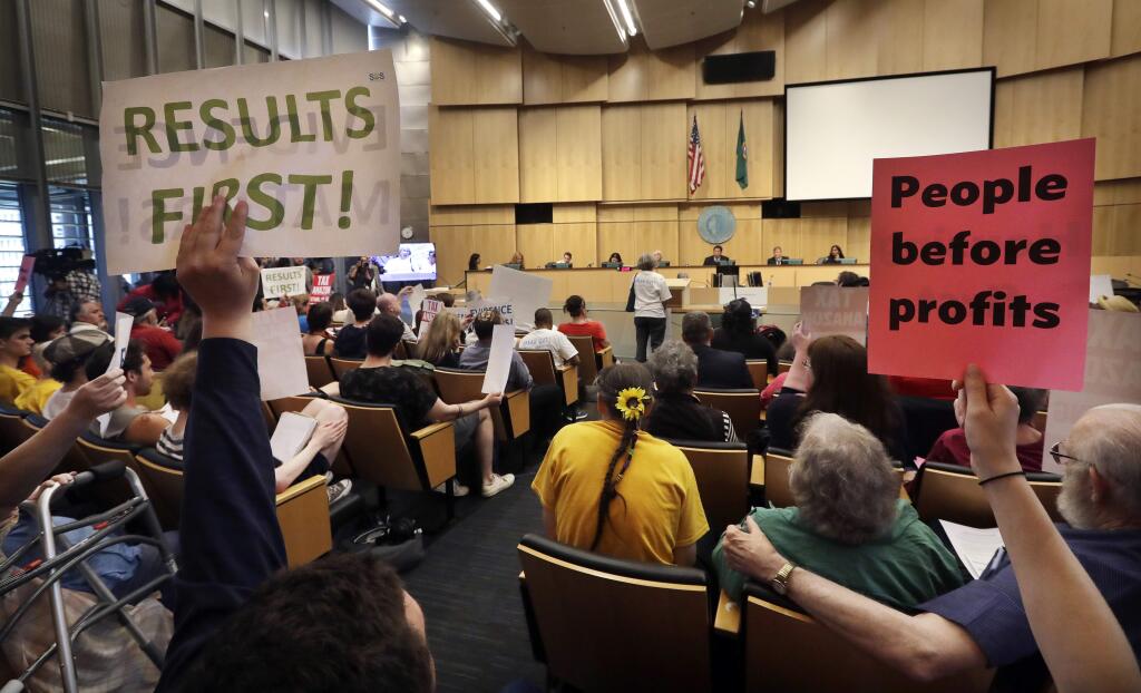 Members of the public look on at a Seattle City Council meeting where the council was expected to vote on a 'head tax' Monday, May 14, 2018, in Seattle. The council is to vote on a proposal to tax large businesses such as Amazon and Starbucks to to raise money to fight homelessness. (AP Photo/Elaine Thompson)