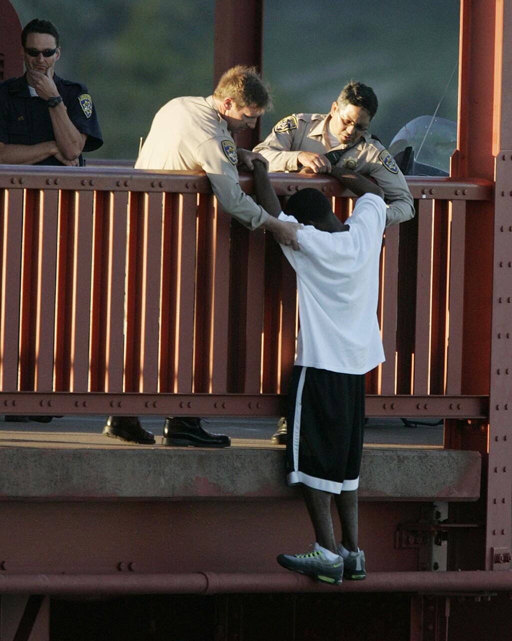 In this March 11, 2005 photo, Kevin Berthia is talked out of jumping off the Golden Gate Bridge and pulled to safety by California Highway Patrolman Kevin Briggs, center, in San Francisco. During his 20 years patrolling the bridge Briggs has managed to talk may despondent people out of taking the fatal fall. On May 8, 2013 the American Foundation for Suicide Prevention will be honoring Sgt. Briggs with their prestigious Public Service Award at an annual Lifesavers dinner in New York City. Berthia has been asked to present Briggs with the award. They have not seen each other since that day, nor has Mr. Berthia had a chance to thank Sgt. Briggs for saving his life. (AP Photo/The San Francisco Chronicle, John Storey)