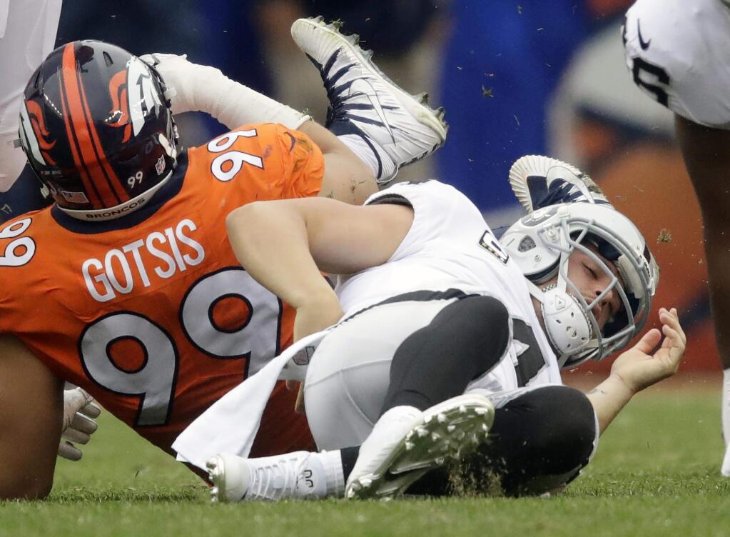 In this photo taken Oct. 1, 2017, Oakland Raiders quarterback Derek Carr, right, grabs his back after being sacked by Denver Broncos defensive ends Adam Gotsis during the second half of an NFL football game in Denver. Carr left the game with a back spasm and the Raiders have more concerns than just his health. (AP Photo/Jack Dempsey)