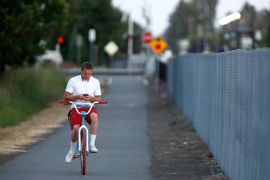 Brandon Simpson of Santa Rosa checks his cell phone while riding his bike along the path running parallel to the SMART train tracks in Rohnert Park, California, on Friday, June 8, 2018. (ALVIN JORNADA/ PD)