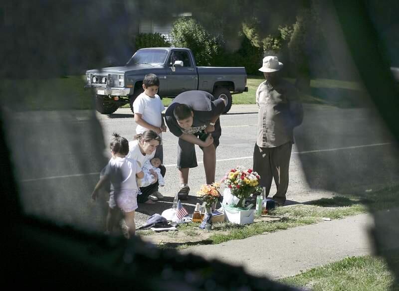 news--3 of 4--In front of her home on South Dora Street in Ukiah, Tuesday April 3, 2007, Shannon Barajas with her three week-old baby Jaime and her brother and law Victor Barajas, 16 and his brother Isidro Barajas, 9, take a closer look at a streetside memorial at the site of where Caesar Mendez, 20, was shot in a furious gun battle between four Ukiah police officers and Mendez Monday. The Barajas family said Mendez was a quiet man. At right is neighborhood resident Carlos Mata. The picture is framed through the pickup window of the Barajas family vehicle which took five bullet holes from police (Kent Porter / The Press Democrat)