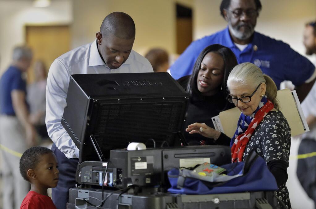 Florida Democratic gubernatorial candidate Andrew Gillum casts his ballot as his wife R. Jai Gillum, second from right, and his son Jackson, lower left, looks on Tuesday, Nov. 6, 2018, in Tallahassee, Fla. Gillum is running against Republican opponent Ron DeSantis. (AP Photo/Chris O'Meara)