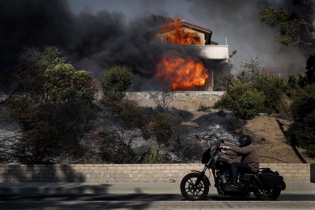 A man rides his bike past the Ventura home of Tubbs fire victim Antonio Wong as it is consumed by wildfire on Tuesday, Dec. 5, 2017. (AP Photo/Jae C. Hong)