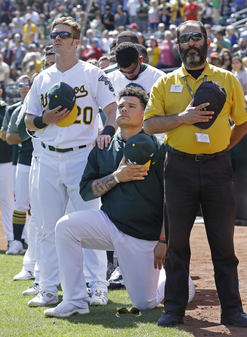 Oakland Athletics' Mark Canha (20) places his hand on the shoulder of Bruce Maxwell as Maxwell takes a knee during the national anthem prior to a baseball game against the Texas Rangers, Sunday, Sept. 24, 2017, in Oakland, Calif. (AP Photo/Ben Margot)