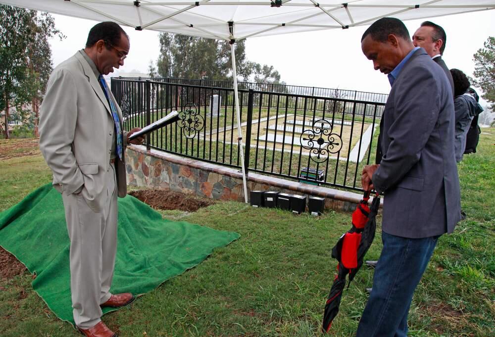 In this Monday, Oct. 20, 2014 photo, Jim Jones Jr., left, son of cult leader Jim Jones, John Cobb, family member of eight Jonestown, Guyana mass suicide-murder victims, right, and Ron Haulman, Executive Director of Evergreen Cemetery, back right, gather for a small memorial as they prepare to inter five Jonestown victim's remains next to the Jonestown memorial at Evergreen Cemetery in Oakland, Calif. Five victims of the 1978 mass suicide-murder in Jonestown, Guyana whose cremated remains were recently discovered inside an abandoned Delaware funeral home were laid to rest Monday in a grave in Oakland where more than 400 other unclaimed or unidentified Jonestown victims are interred. (AP Photo/Bay Area News Group, Laura A. Oda)