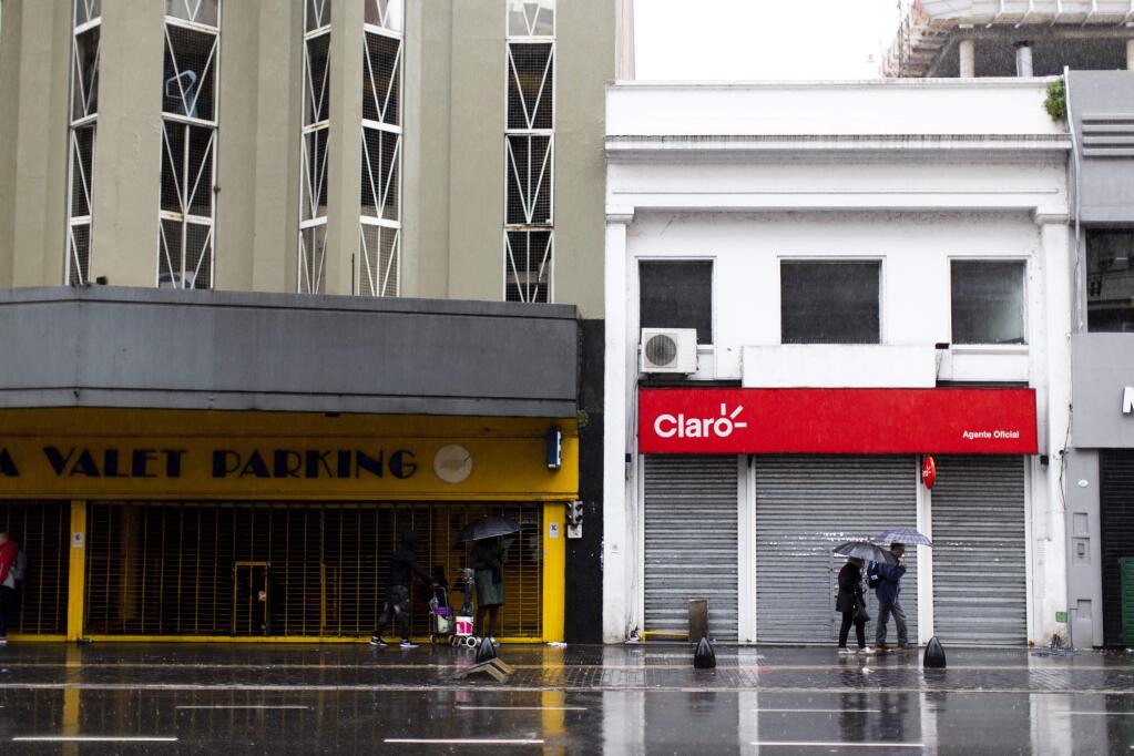 People walk in front of closed stores during a blackout, in Buenos Aires, Argentina, Sunday, June 16, 2019. Argentina and Uruguay were working frantically to return power on Sunday, after a massive power failure left large swaths of the South American countries in the dark. (AP Photo/Tomas F. Cuesta)
