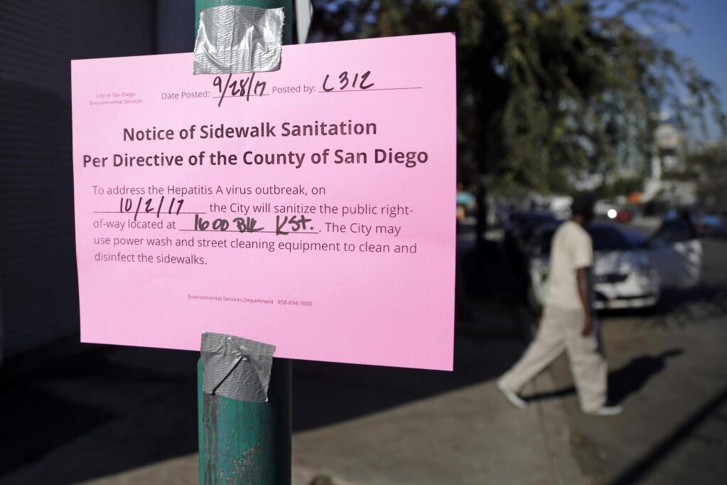 FILE - In this Sept. 28, 2017 file photo a man passes behind a sign warning of an upcoming street cleaning in San Diego. Health officials say a deadly California outbreak of hepatitis A may take a year or more to abate. The liver-damaging illness has infected hundreds of people since last November, chiefly in San Diego, Santa Cruz and Los Angeles counties. Most cases and all 17 deaths occurred in San Diego County. Experts believe the highly contagious disease was spread by transients there to homeless populations around the state. (AP Photo/Gregory Bull, File)