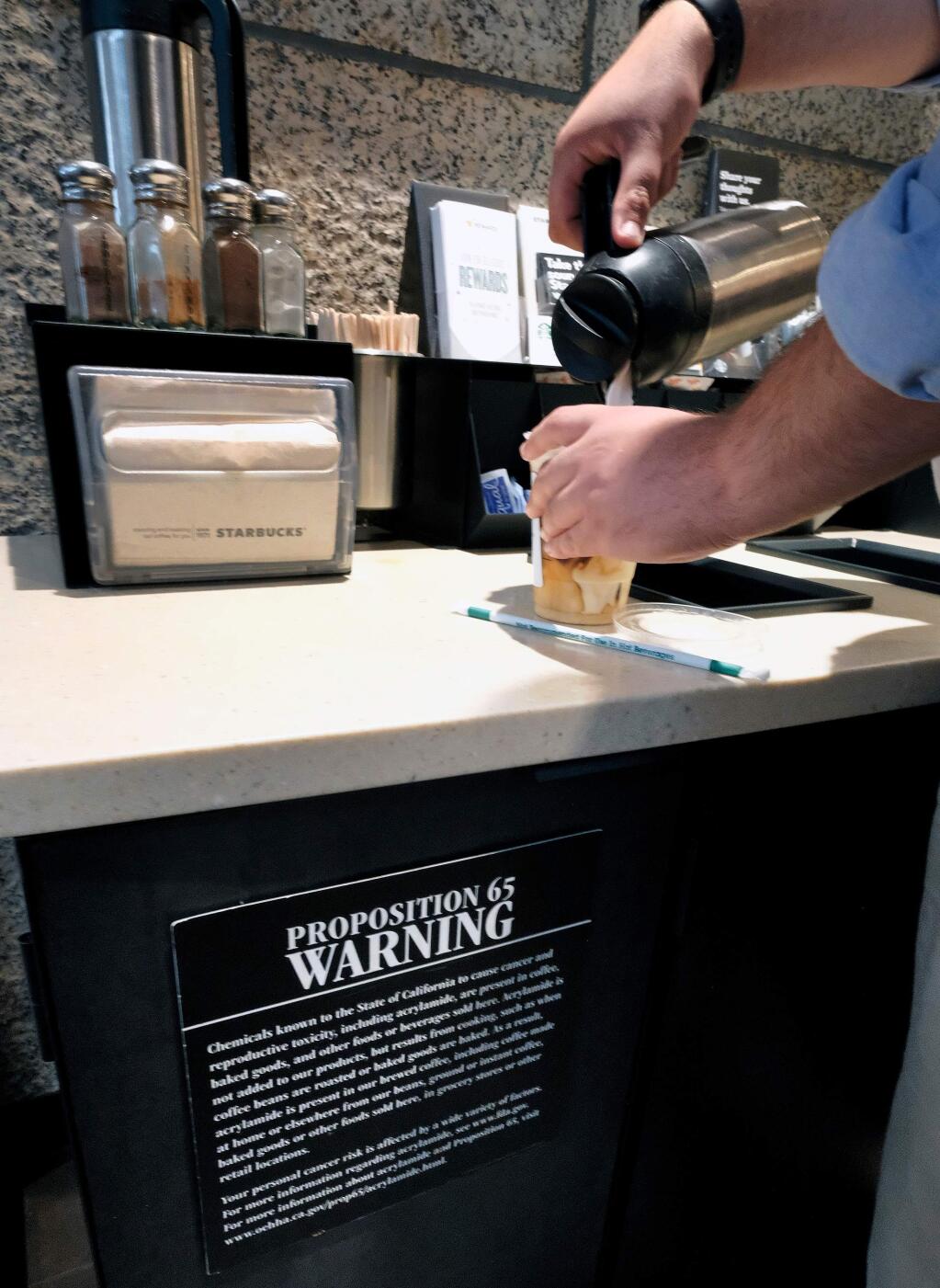 FILE -In In this Sept. 22, 2017, file photo, a customer pours milk into coffee near a posted Proposition 65 warning sign at a Starbucks coffee shop in Los Angeles. Superior Court Judge Elihu Berle has ruled that California law requires coffee companies to carry an ominous cancer warning label because of a chemical produced in the roasting process. Judge Berle wrote in a proposed ruling Wednesday, March 28, 2018, that Starbucks and other coffee companies failed to show that the threat from a chemical compound produced in the roasting process was insignificant. At the center of the dispute is acrylamide, a carcinogen found in many cooked foods, that is produced during the roasting process. (AP Photo/Richard Vogel)