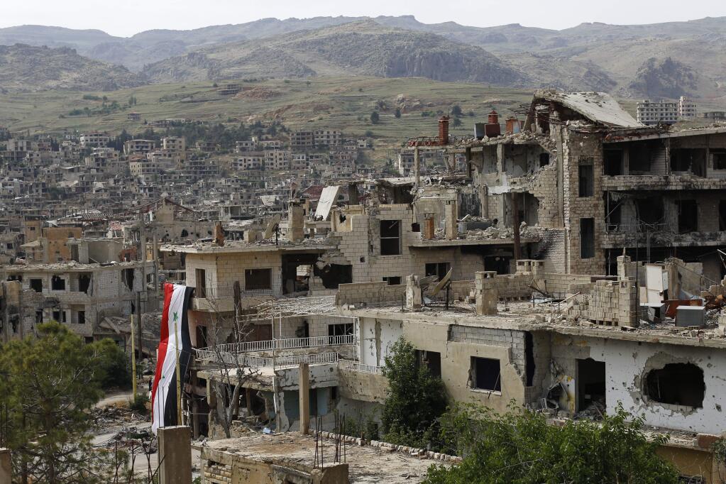 FILE - In this May 18, 2017 file photo, a Syrian National flag hangs out of a damaged building at the mountain resort town of Zabadani in the Damascus countryside, Syria. The Syrian government on Tuesday, June 27, 2017 dismissed White House allegations that it was preparing a new chemical weapons attack, as activists reported an airstrike on an Islamic State-run jail in eastern Syria that they said killed more than 40 prisoners. (AP Photo/Hassan Ammar, File)