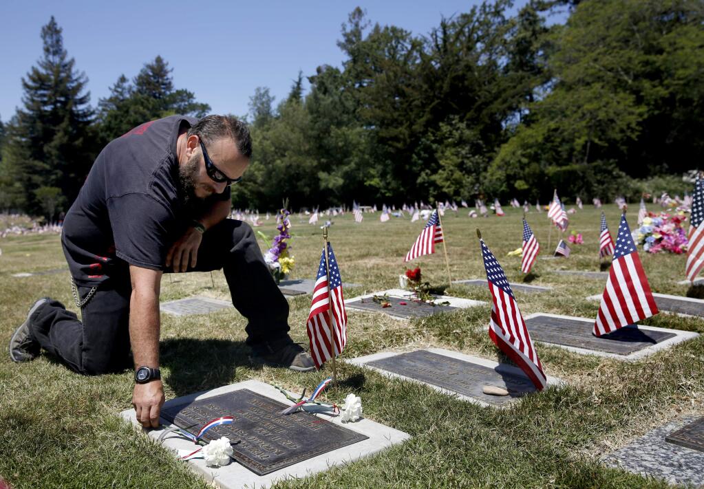 Good Ol' Boys motorcycle club member and Army veteran Darrell Ottolini places two carnations at the grave of his grandfather Daniel Ottolini, a WWII Army veteran, to remember him and his father Michael Ottolini, who was killed serving in the Army in Iraq in 2004. The 4th annual Veterans Bike Run, stopped at Santa Rosa Memorial Park after leaving the Veterans Memorial Building in Santa Rosa, on Sunday, May 24, 2015. (BETH SCHLANKER/ The Press Democrat)