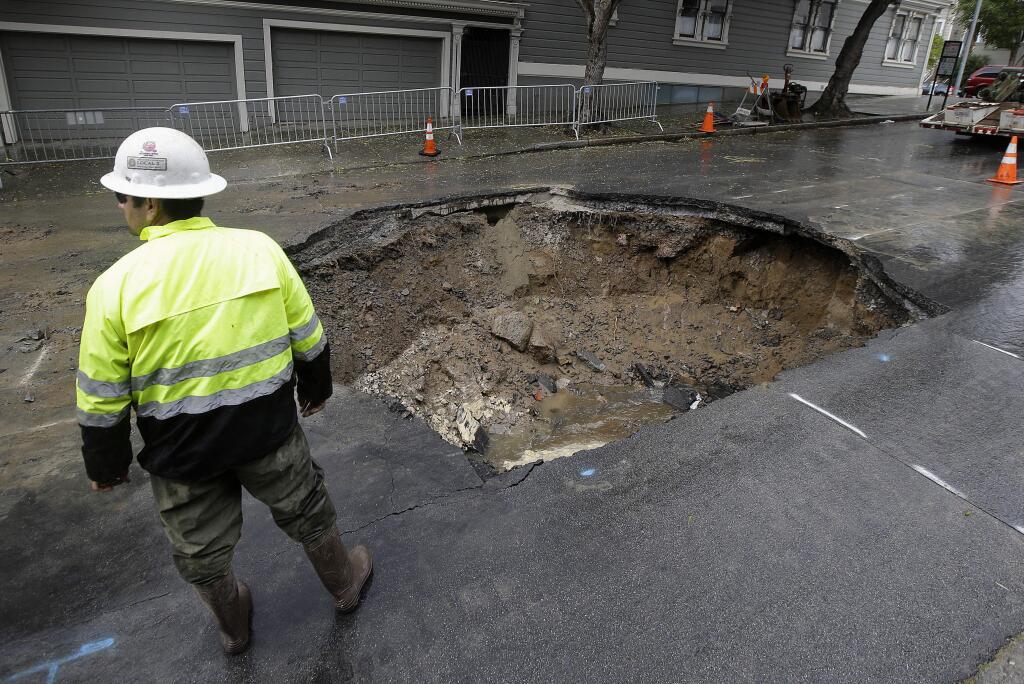 A San Francisco Public Utilities Commission worker stands over a large sinkhole on Sacramento Street in San Francisco, Friday, April 22, 2016. According to a spokesperson for the the city's Public Utilities Commission, the sinkhole appeared on Thursday, caused by a broken sewer pipe line. (AP Photo/Jeff Chiu)