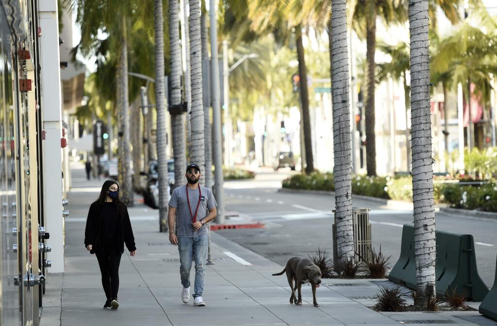 A couple walks a dog down a nearly empty Rodeo Drive as stay-at-home orders continue in California due to the coronavirus, Monday, March 30, 2020, in Beverly Hills, Calif. (AP Photo/Chris Pizzello)