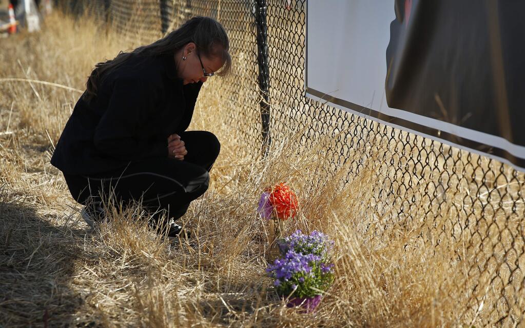 Robin Griffiths, of Portland, prays at a makeshift memorial near the road leading to Umpqua Community College Saturday, Oct. 3, 2015, in Roseburg, Ore. Armed with multiple guns, Chris Harper Mercer, 26, walked in a classroom at the community college, Thursday, and opened fire, killing several and wounding several others. (AP Photo/John Locher)