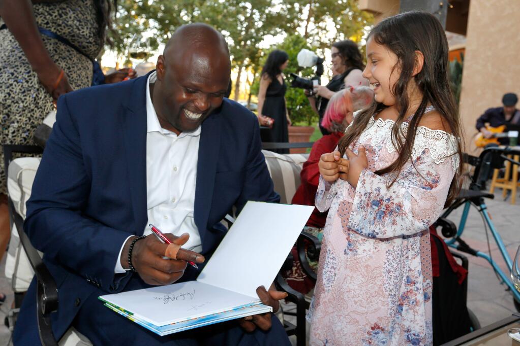 Retired NBA player Adonal Foyle, the event keynote speaker, laughs with Khloe Campbell, 7, as he autographs a children's book he wrote, during the Lime Foundation's Believe in the Dream gala at Vintner's Inn, in Santa Rosa, California, on Thursday, September 13, 2018. (Alvin Jornada / The Press Democrat)