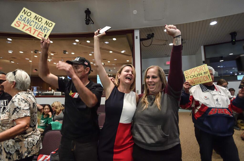 FILE - In this March 27, 2018, file photo, David Hernandez, left, Genevieve Peters, center, and Jennifer Martinez celebrate after the Orange County Board of Supervisors voted to join the U.S. Department of Justice lawsuit against the State of California's sanctuary cities law during their meeting in Santa Ana, Calif. A federal judge has dismissed the federal government's claim that U.S. law trumps two California laws intended to protect immigrants who are in the country illegally. The ruling by U.S. District Judge John Mendez follows his ruling last week that found California was within its rights to pass two of the three sanctuary laws. He ruled Monday, July 9, 2018, that the federal government could proceed with its attempt to block part of a third California sanctuary law. (Jeff Gritchen/The Orange County Register via AP, File)