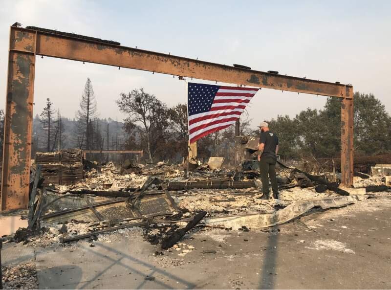 PRESS DEMOCRAT PHOTOJonny Gomes stands under a flag and the frame of a burned out house belonging to Sonoma County Sheriff's Deputy Ken Johnson.