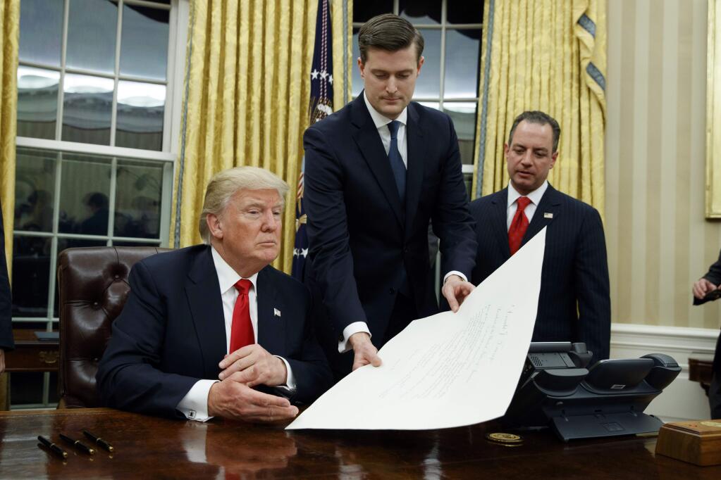 FILE - In this Jan. 20, 2017 file photo, White House Staff Secretary Rob Porter, center, hands President Donald Trump a confirmation order for James Mattis as defense secretary, in the Oval Office of the White House in Washington, as White House Chief of Staff Reince Priebus, right, watches. Porter is stepping down following allegations of domestic abuse by his two ex-wives. (AP Photo/Evan Vucci)