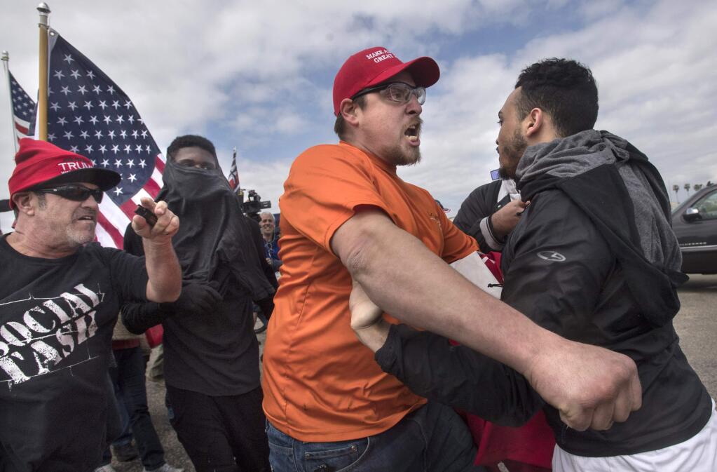 A supporter of President Donald Trump, center, clashes with an anti-Trump protester in Huntington Beach, Calif., on Saturday, March 25, 2017. Counter-protesters said before the march began that they planned to try to stop the march's progress with a 'human wall.' (Mindy Schauer/The Orange County Register via AP)