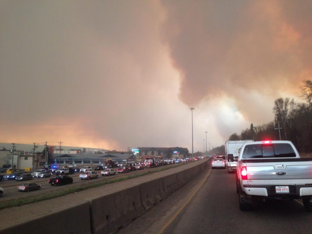 Smoke from a wildfire rises in the air as cars line up on a road in Fort McMurray, Alberta, Tuesday, May 3, 2016. At least half of a northern Alberta city was ordered evacuated Tuesday as a wildfire whipped by winds engulfed homes and sent ash raining down on residents. (Greg Halinda/The Canadian Press via AP)