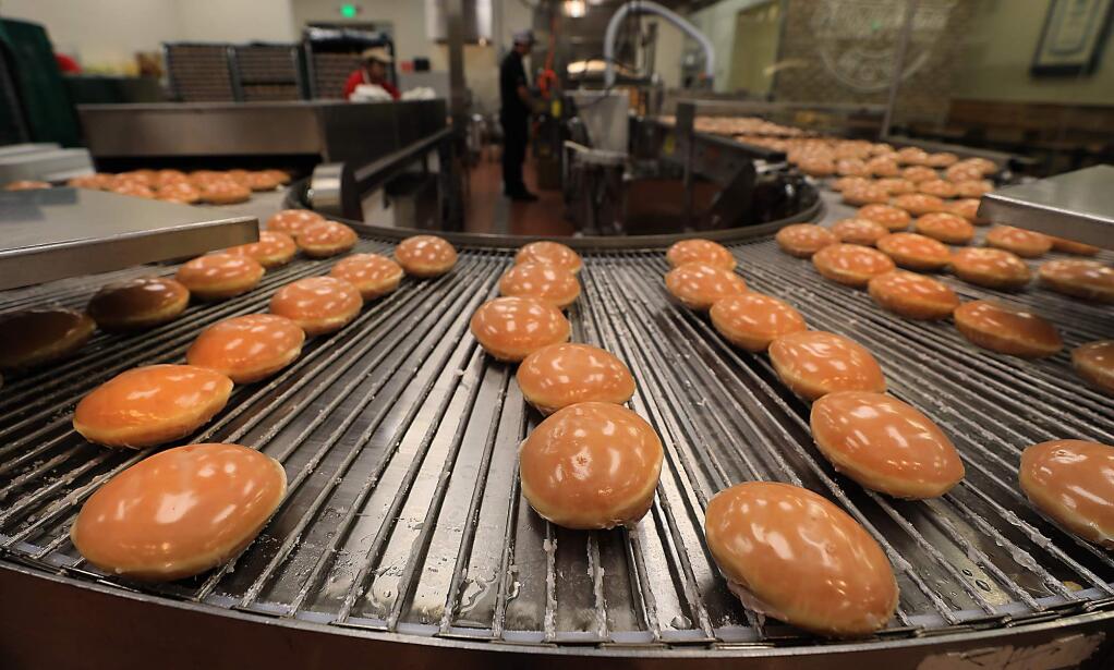 Doughnuts are passed through a glaze prior to the grand opening of the Krispy Kreme in Rohnert Park on Monday, Nov. 5, 2018. (KENT PORTER/ PD)