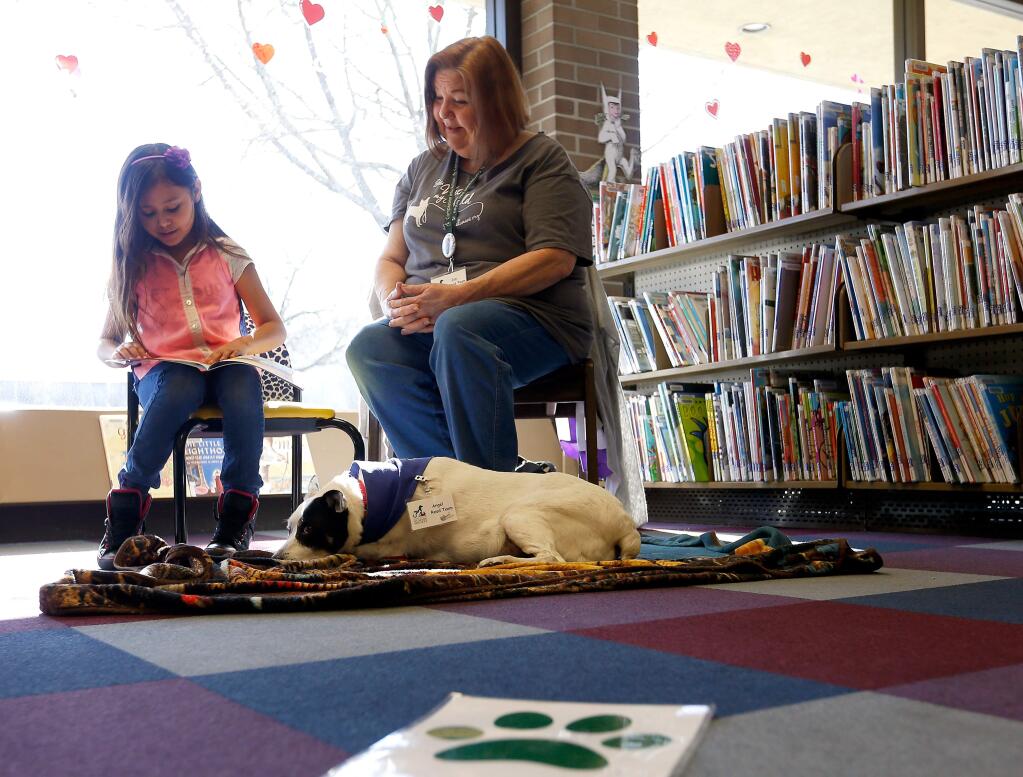 Maggie Hernandez, 7, left, reads aloud to Angel the dog and volunteer Jan Nagy of the Sonoma County Humane Society during the Read to a Dog program at the Central Santa Rosa Library in Santa Rosa, California on Saturday, Feb. 11, 2017. (Alvin Jornada / The Press Democrat)