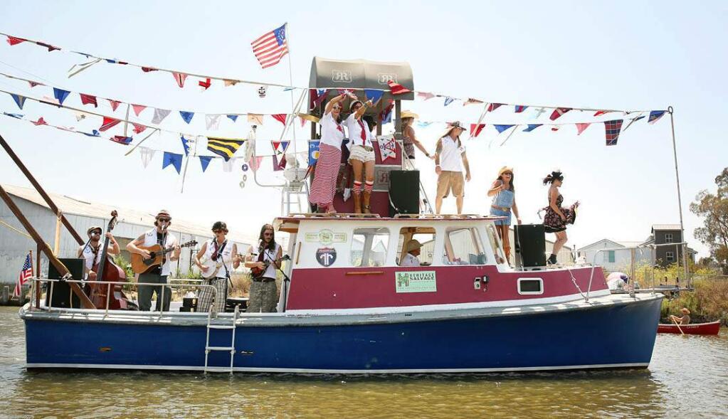 Members of the band Highway Poets and revelers perform on a boat as it passes by the crowds gathered for the Rivertown Revival in Petaluma, July 20, 2013. (Conner Jay / Press Democrat)