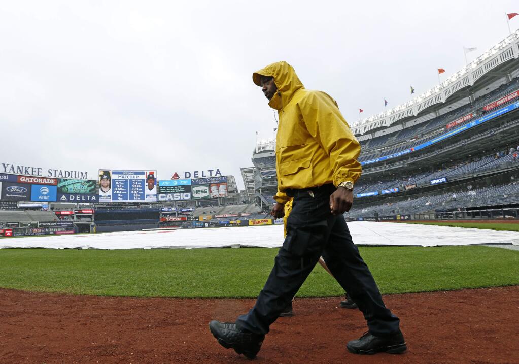 A security guard walks on a tarp-covered field before the scheduled start of a baseball game between the New York Yankees and the Oakland Athletics in New York, Sunday, May 13, 2018. (AP Photo/Kathy Willens)