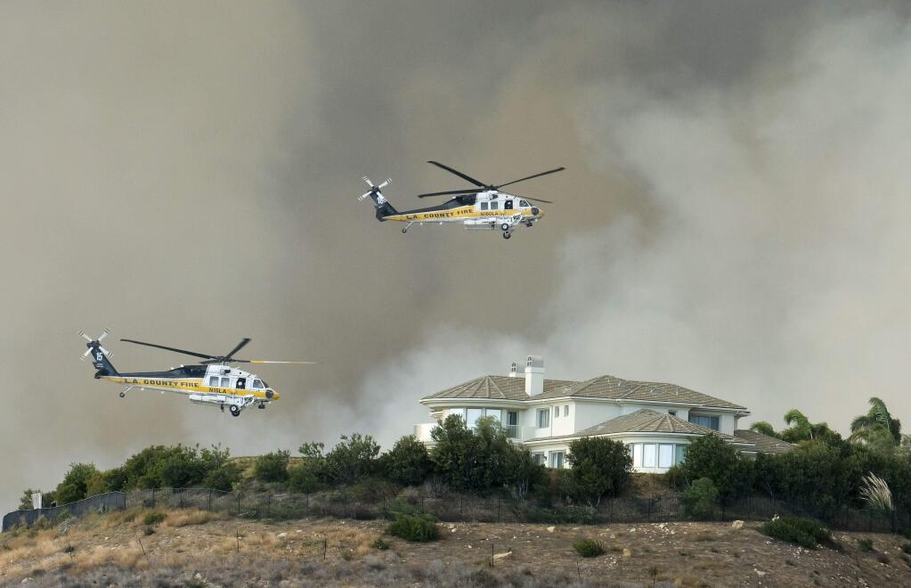 Helicopters prepare to drop water on a brush fire behind a home during the Woolsey Fire in Malibu. (RINGO H.W. CHIU / Associated Press)
