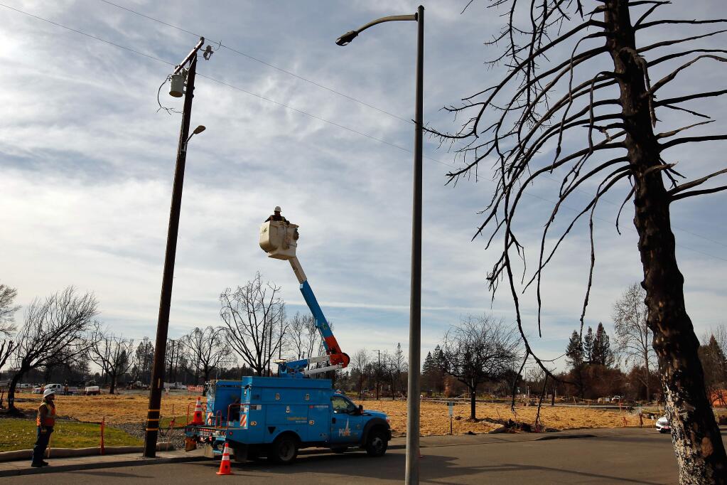 PG&E foreman Freddy Garcia and preapprentice lineman Quienton Smith, lower left, finish installing a temporary streetlight, across the street from a fire-damaged streetlight and burned tree on Jean Marie Drive in the Mark West Estates neighborhood of Santa Rosa, California on Saturday, December 30, 2017. (Alvin Jornada / The Press Democrat)