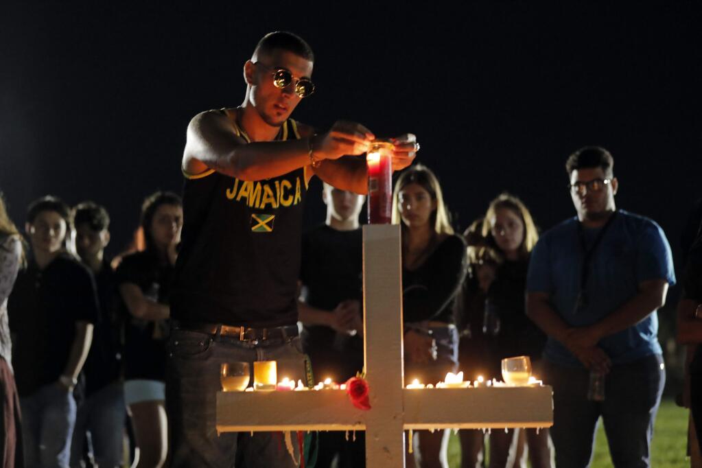 Joey Kandil, 18, a recent graduate of Marjory Stoneman Douglas High School, places a ring around a candle on one of seventeen crosses, after a candlelight vigil for the victims of the Wednesday shooting at the school, in Parkland, Fla., Thursday, Feb. 15, 2018. Nikolas Cruz, a former student, was charged with 17 counts of premeditated murder on Thursday. (AP Photo/Gerald Herbert)