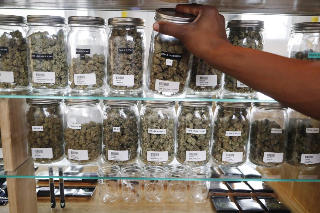FILE - In this Oct. 2, 2018, file photo, a clerk reaches for a container of marijuana buds for a customer at Utopia Gardens, a medical marijuana dispensary in Detroit. Chronic pain is the most commonly cited reason people give when they enroll in state medical cannabis programs. A study published Monday, Feb. 4, 2019, in the journal Health Affairs looks at available data from states that allow marijuana for medical use. (AP Photo/Carlos Osorio, File)