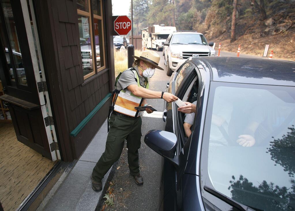 Park Ranger Anne Simmons passes maps out and directs visitors at the Hwy 140 gate as Yosemite National Park reopens after a three week closure from smoke and fires that led to most tourists canceling their trips Tuesday, Aug. 14, 2018 in Yosemite, Calif. (AP Photo/Gary Kazanjian)
