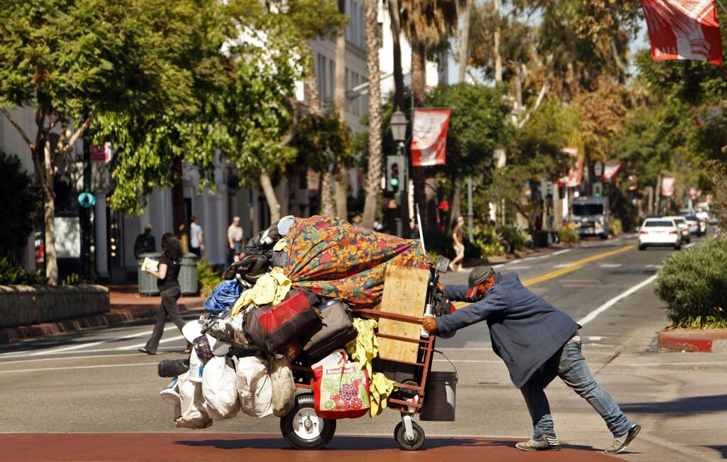 A homeless man pushes a huge cart of belongs across State Street in Santa Barbara. (AL SEIB / Los Angeles Times)