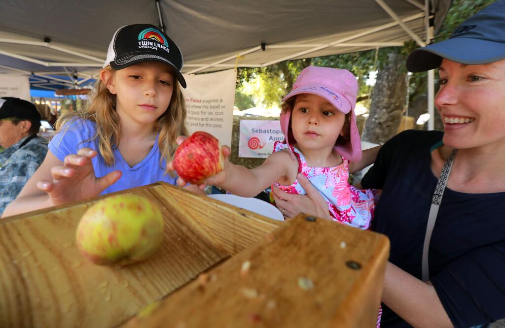 From right, Leah Ble, helps her children Josie, 2, and Sophia, 7, load apples into the community press at the Gravenstein Apple Fair at Sebastopol's Ragle Ranch Park. (photo by John Burgess/The Press Democrat)