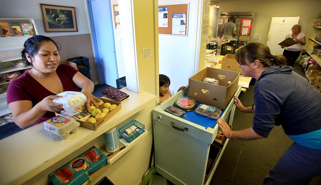 At F.I.S.H. (Friends In Service Here), Alejandra Cruz-Lopez obtains free groceries from Jennifer Hornbeck of St. Patrick's Church as Hornbeck interacts with Cruz's daughter Andrea, Thursday October 15, 2015. (Kent Porter / Press Democrat) 2015