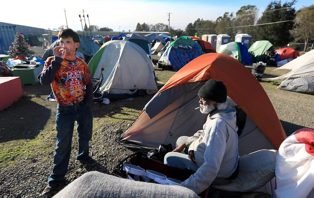 Timothy Raymond, left and Alamando Cooper share a smoke, Monday Dec. 11, 2017 in Roseland, as the homeless camp continues to swell. Raymond is not a resident of the camp. County officials are discussing moving the camp, due to the development of Roseland Village to be built on the spot of the encampment. (Kent Porter / Press Democrat) 2017