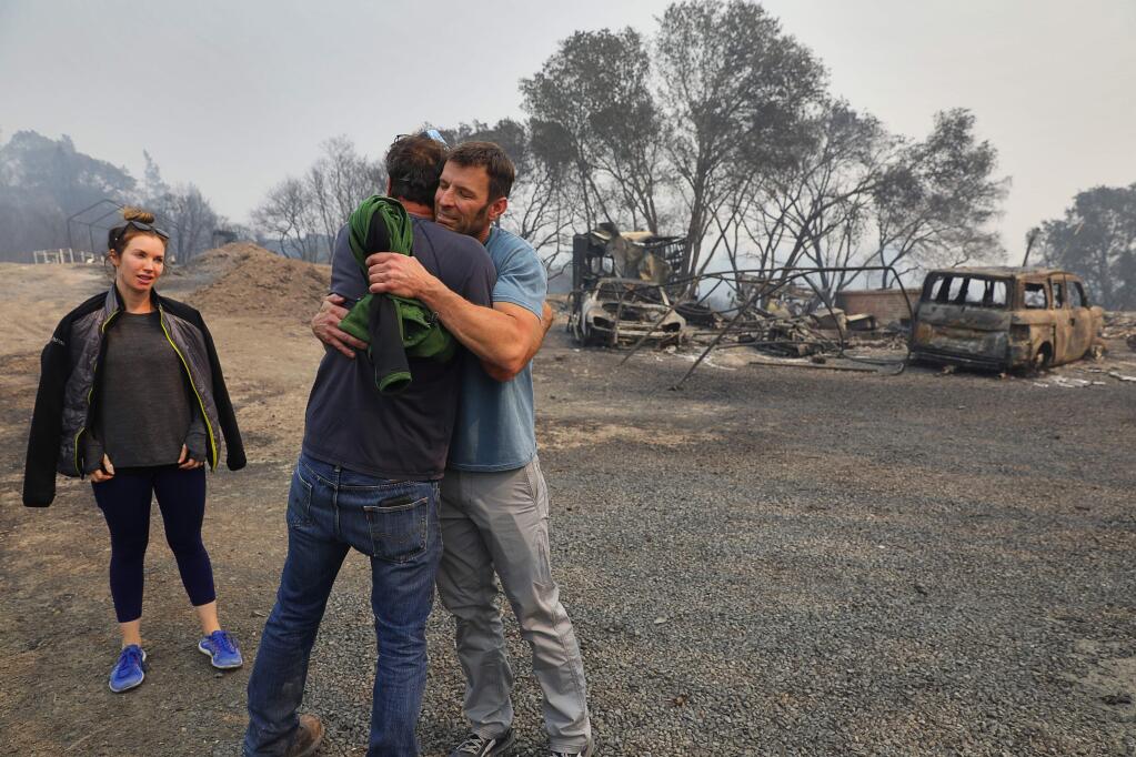 Brian White, right, and his Mark West Springs Road neighbor Mike Nunley hug, as his girlfriend Cher Jeffers looks on, while at the burned remnants of his home, near Santa Rosa on Tuesday, October 10, 2017. White is a Santa Rosa Fire Department firefighter who was battling the fires in the Fountaingrove area, while his house was destroyed. (Christopher Chung/ The Press Democrat)