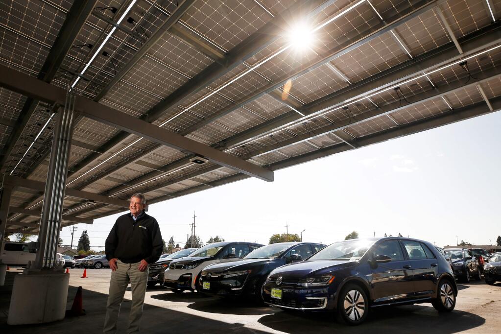 Henry Hansel, president of Hansel Auto Group, poses for a portrait beneath an array of solar panels at Hansel Ford, with a row of various hybrid and electric cars sold by his car dealerships, in Santa Rosa, California, on Thursday, September 19, 2019. (Alvin Jornada / The Press Democrat)