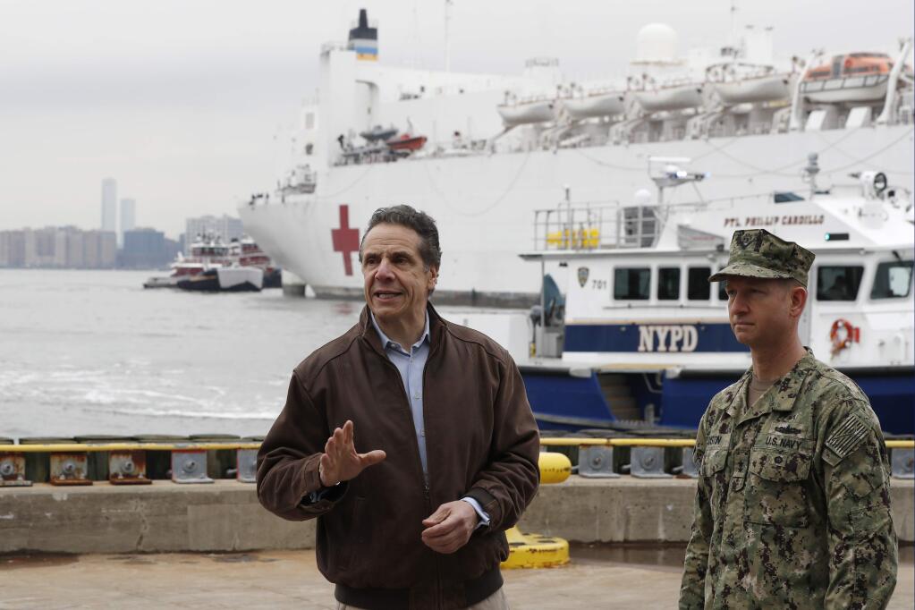 New York Gov. Andrew Cuomo, left, gestures during a brief news conference as he stands beside a Rear Adm. John B. Mustin as the USNS Comfort, a naval hospital ship with a 1,000 bed-capacity, pulls into Pier 90 Monday, March 30, 2020, in New York. The ship will be used to treat New Yorkers who don't have coronavirus as land-based hospitals fill up with and treat those who do. (AP Photo/Kathy Willens)