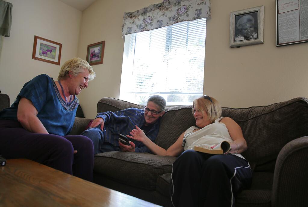 Crystal Naef, left, Toni Beccaria, and Brooke Schwinn laugh while playing a game on a smartphone together in the community area of the Sloan House women's shelter in Santa Rosa on Monday, March 13, 2017. (Christopher Chung/ The Press Democrat)