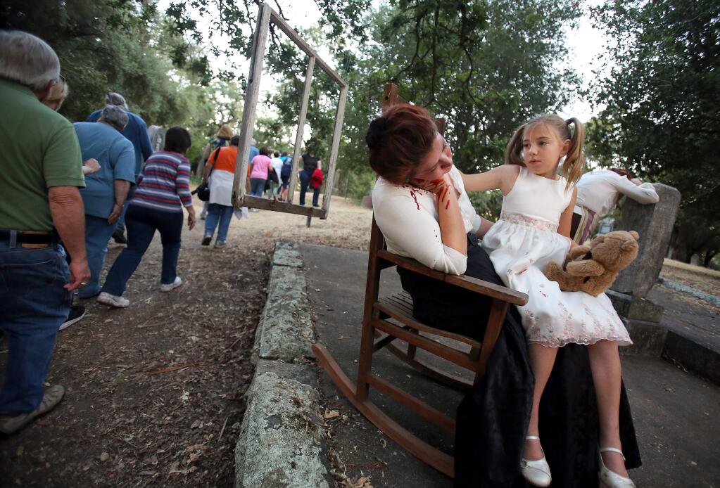 Guests walk past a theatrical reenactment of the murder of Luella May Butts played by Amy Lovato, center, sitting on her lap is her daughter Helen Butts played by Maisy Gibson during The Dark Side of the Cemetery tour at Santa Rosa Rural Cemetery Friday, June 13, 2014. Butts was murdered by her husband Claude Butts in 1913 who was sentenced to five years in prison for the murder. He then moved to the Yreka area and remarried. He died in 1968 at the age of 81. (Crista Jeremiason / The Press Democrat)