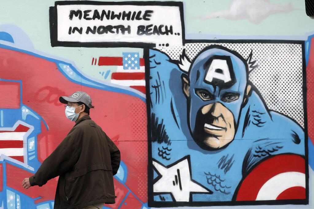 A man wears a face mask while walking past an image of Captain America outside of a boarded up liquor store during the coronavirus outbreak in San Francisco, Tuesday, May 12, 2020. (AP Photo/Jeff Chiu)