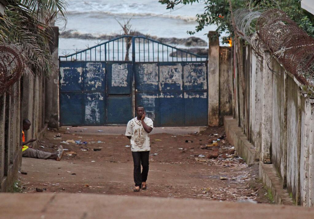 A man, center, walks past the entrance to the property, seen left where a man is sitting, where a stampede took place the night before during a rap concert in the city of Conakry , Guinea, Wednesday, July 30, 2014. Hundreds of people leaving a late-night rap concert on a beach in Guinea rushed to leave through a single exit, creating a stampede that killed at least 33 people, officials said Wednesday. The victims included children as young as 10, and most bodies brought to an overflowing morgue in the capital were still dressed in bathing suits and swim trunks. (AP Photo/ Youssouf Bah)