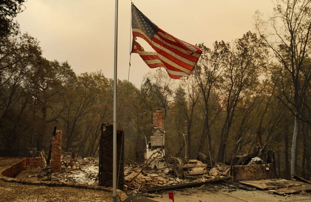 A tattered flag flies over a burned out home at the Camp Fire, Sunday, Nov. 11, 2018, in Paradise, Calif. (AP Photo/John Locher)
